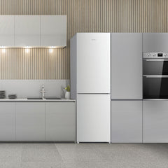 Modern kitchen with light gray cabinets, a Statesman v60/40 Low Frost Fridge Freezer in White by Statesman Appliances, built-in oven, sink, stovetop, and dishes on the counter. The wall features vertical wooden slats and under-cabinet lighting, while adjustable shelving ensures flexible storage options.