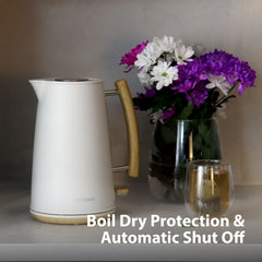 A Statesman Appliances 1.7L Scandi Kettle with wooden handle sits on a counter near a glass vase of purple and white flowers and a cup. Text: Rapid Boil, Cordless Base, Boil Dry Protection & Auto Shut Off.