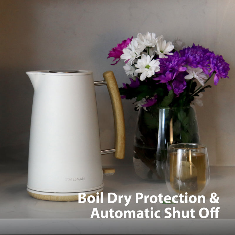 A Statesman Appliances 1.7L Scandi Kettle with wooden handle sits on a counter near a glass vase of purple and white flowers and a cup. Text: Rapid Boil, Cordless Base, Boil Dry Protection & Auto Shut Off.