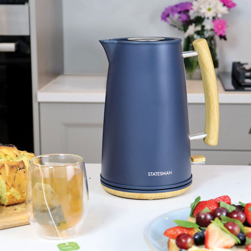 The Statesman Appliances 1.7L Scandi Kettle, featuring a cordless base and 3000W power, sits on a kitchen counter near tea, fruit, bread, and flowers.