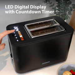 A person touches the LED display on the Statesman 900W 2 Slice Digital Toaster by Statesman Appliances. The black toaster’s wide slots are visible, and the display shows a countdown timer with text above: “LED Digital Display with Countdown Timer.”.