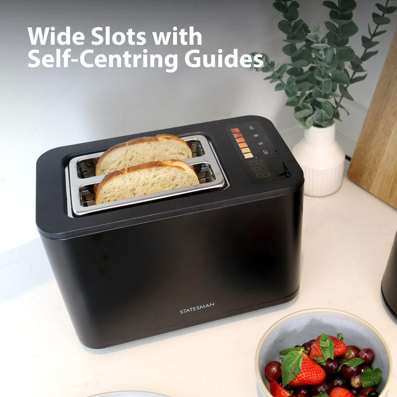 The Statesman 900W 2 Slice Digital Toaster from Statesman Appliances sits on a kitchen counter beside strawberries and blueberries, its sleek black design with wide slots, self-centring guides, and LED display ready for breakfast.