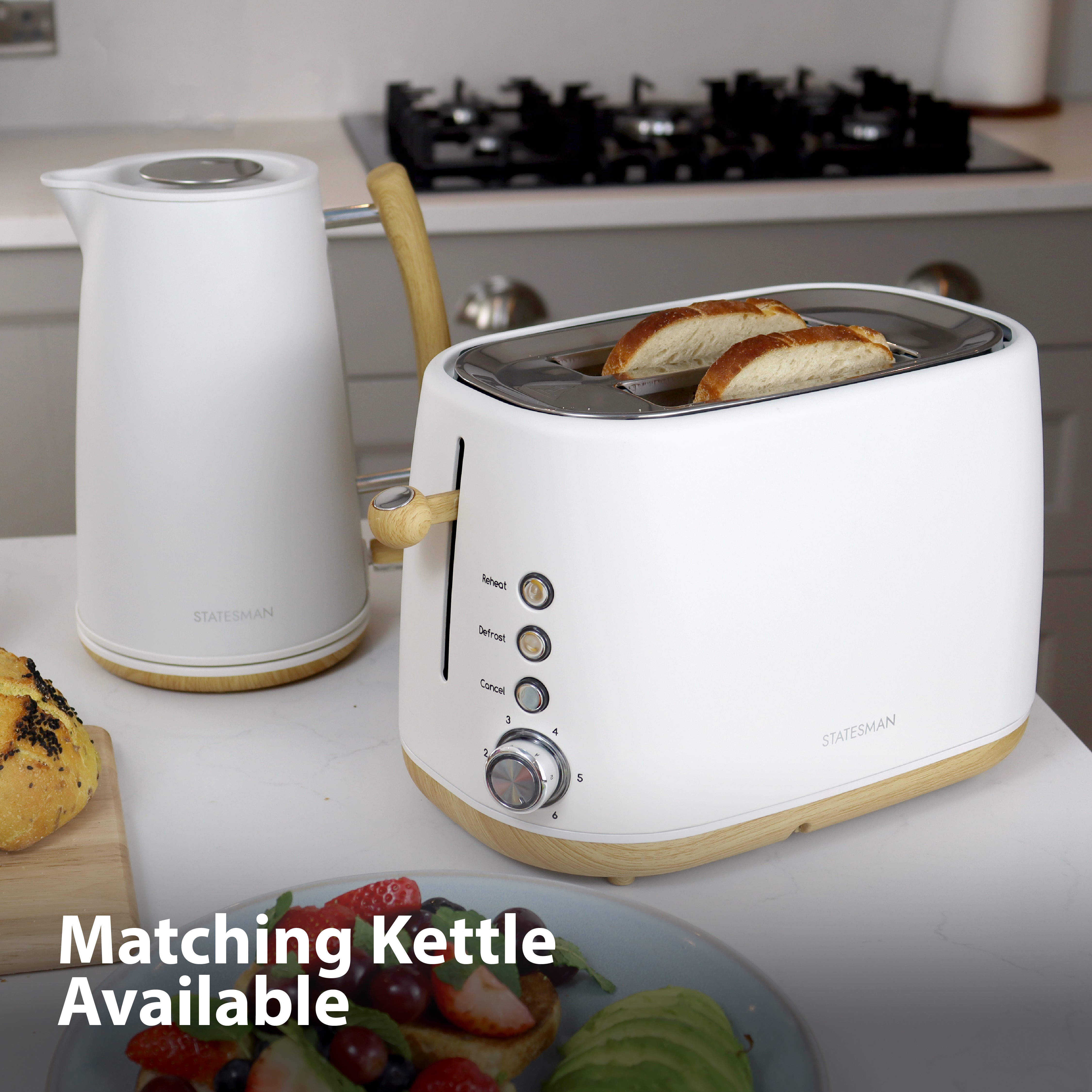 A Statesman Appliances 900W 2 Slice Scandi Toaster with bread and a matching white electric kettle sit on the counter. Text reads "Matching Kettle Available." A stove and food items are in the background.