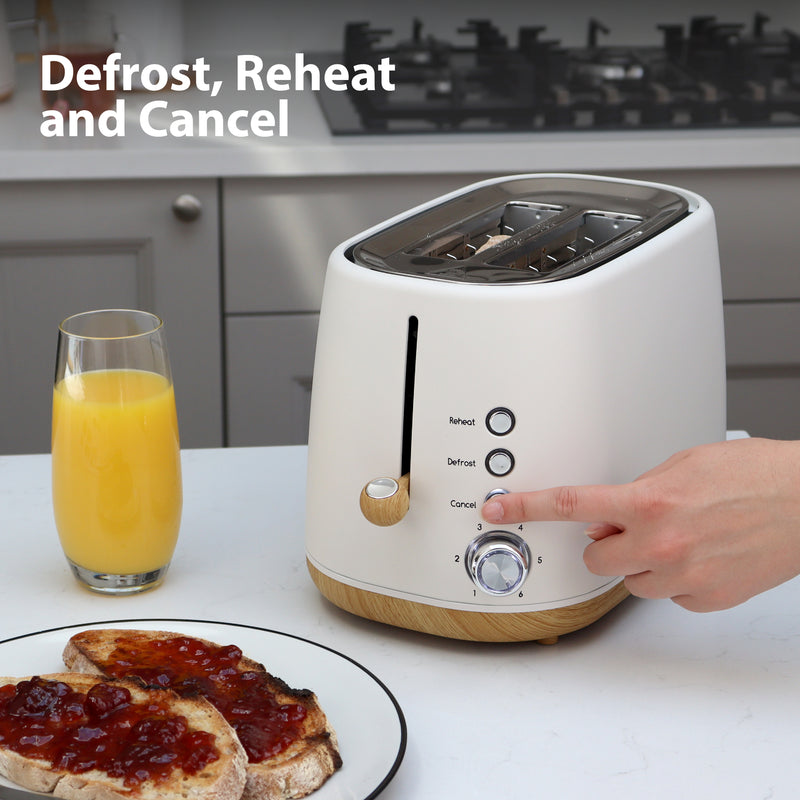 A hand presses a button on the white Statesman 900W 2 Slice Scandi Toaster from Statesman Appliances, labeled Reheat, Defrost, and Cancel. Nearby are a glass of orange juice and two slices of jam toast. "Defrost, Reheat and Cancel" tops the scene.